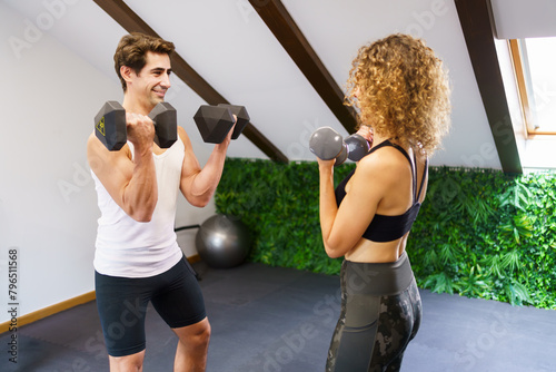 Strong sportswoman lifting dumbbells with personal trainer