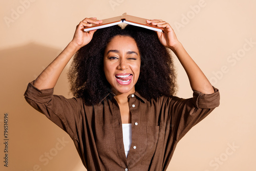 Photo of flirty girl with perming coiffure wear brown blouse holding book on head winking lick teeth isolated on pastel color background