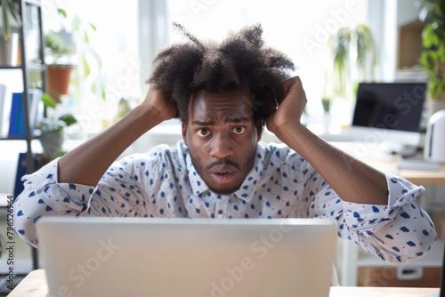 A confused Afro-American man stares perplexedly at his computer screen, appearing frustrated as he grapples with complex information or attempts to troubleshoot a software issue. photo