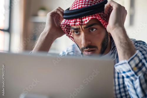 A perplexed Arab man stares at his computer screen, looking baffled and frustrated as he attempts to grasp complex information or rectify a software glitch photo
