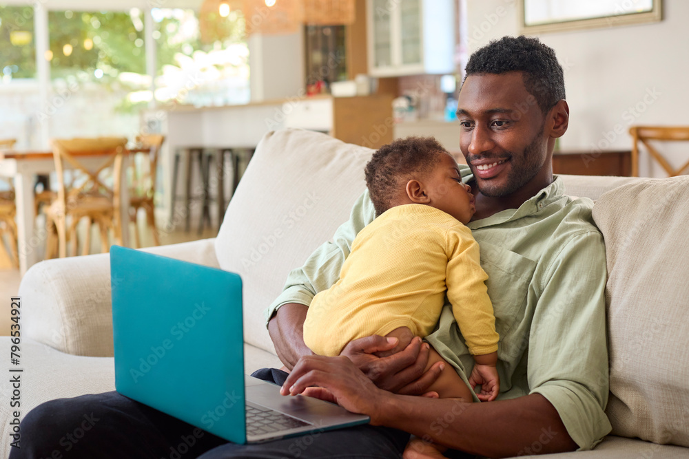Family With Father Working On Laptop Cuddling Sleeping Baby Daughter On Sofa At Home Family With Father Working On Laptop Cuddling Sleeping Baby Daughter On Sofa At Home