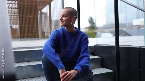 modern shaved woman sitting on stairs contemplating the horizon with skyscrapers