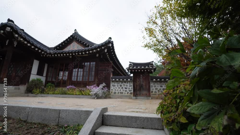 a traditional Korean house, known as a Hanok, with tiled roofs, wooden beams, white walls, and a stone base, surrounded by lush greenery under a cloudy sky. a traditional Korean house, known as a Hanok, with tiled roofs, wooden beams, white walls, and a stone base, surrounded by lush greenery under a cloudy sky.