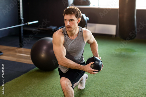 Young strong man exercising with medicine ball in gym, having morning workout photo