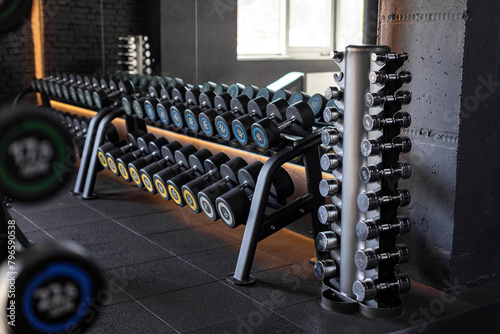Stand with various dumbbells, weight training equipment, black dumbbell set on rack in modern sport fitness center