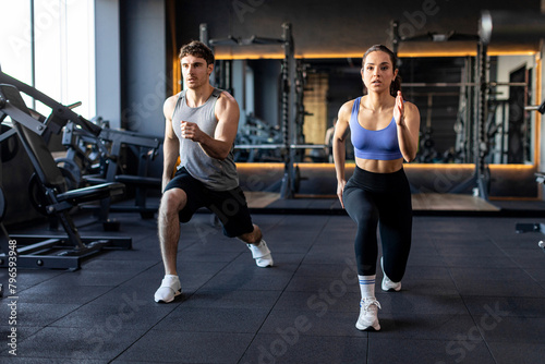 Personal training for two. Fitness man and woman do lunges exercises to warm up and burn leg muscles, modern gym interior