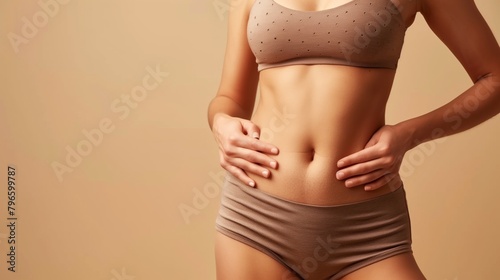 Close-up of a woman in beige sportswear showing her fit midsection on a neutral background.
