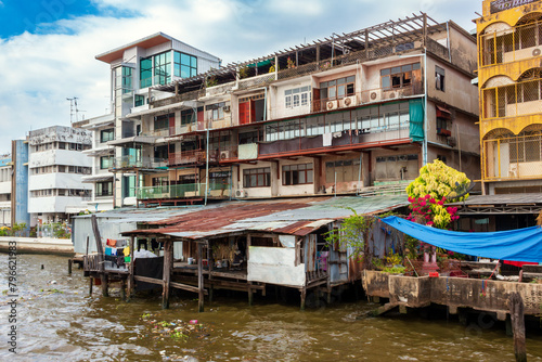 Cityscape with collapsing wooden residential slums on stilts against the backdrop of old and modern concrete buildings on the Chao Phraya River in Bangkok, Thailand. Real local life in Asia
