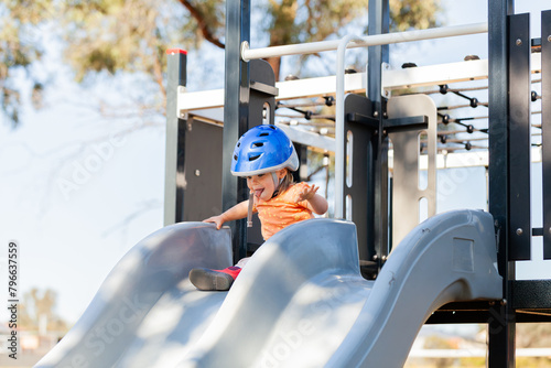 Toddler sticking tongue out while sliding down slide at park photo