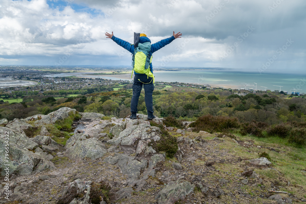 Hiker raises his arms in the air after reaching the top of the mountain