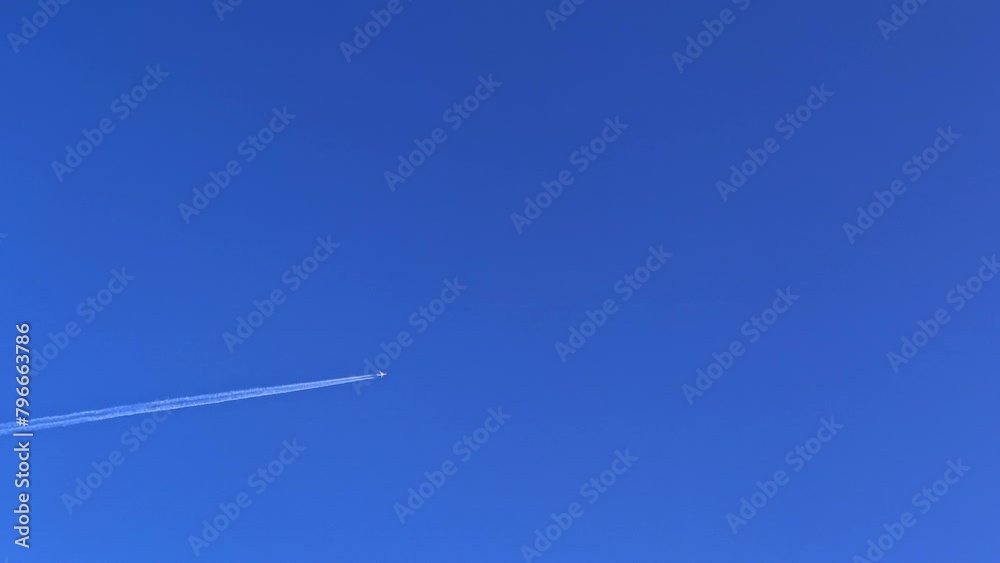 An airplane flying with jet contrail stretching and crossing the clear and blue sky. Cloudscape with blue sky background. An airplane flying with jet contrail stretching and crossing the clear and blue sky. Cloudscape with blue sky background.