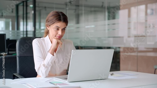 Busy mature middle aged professional business woman manager executive looking at laptop working on computer in office thinking of digital market plan or considering new corporate idea sitting at desk.