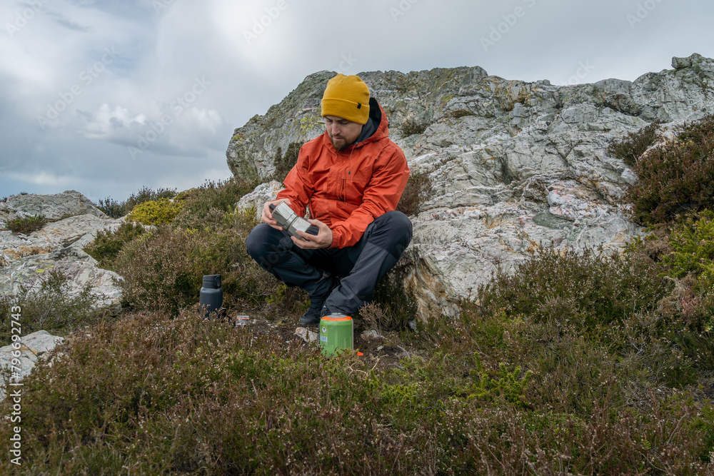 Mountain climber sitting on rock, rests while preparing coffee in stovetop coffee maker Mountain climber sitting on rock, rests while preparing coffee in stovetop coffee maker