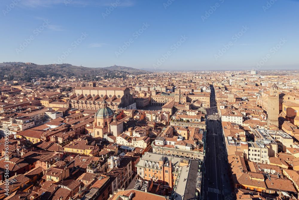 Naklejka premium A panoramic view of Bologna historic city center from above. The red-tiled rooftops and cathedral domes create a picturesque scene, with hills on the horizon
