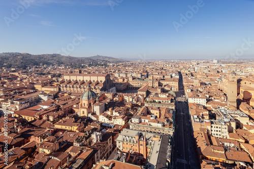 A panoramic view of Bologna historic city center from above. The red-tiled rooftops and cathedral domes create a picturesque scene, with hills on the horizon