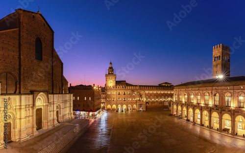 Sunset light bathes Piazza Maggiore in Bologna, highlighting the grandeur of its medieval structures against the dusk sky