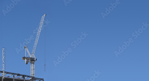 Hoisting tower crane on the top section being constructed of modern high skyscraper building against blue cloudless sky with large free space on photo