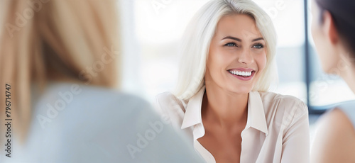 Positive Company Cultureю Happy Coworkers Discuss Project in Bright Office Space During Meeting. Teamwork Concept. Smiling Businesswoman Engages in Conversation with Colleagues During Team Meeting.