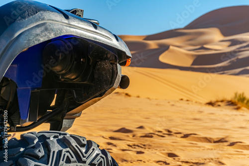A four wheeled quad front part blue and black color vehicle parked  in the Sahara desert, selective focus in foreground, sunny day with golden yellow colored sand dunes and blue sky in blur background