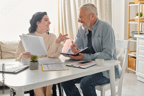 A man and a disabled woman in a wheelchair sit at a table, engaged in deep conversation in their kitchen at home.