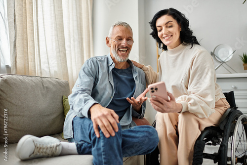 A man sits next to his wife on a wheelchair with smartphone in a cozy living room. photo