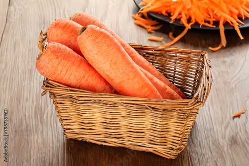 Peeled sweet carrots in a basket on a wooden table.