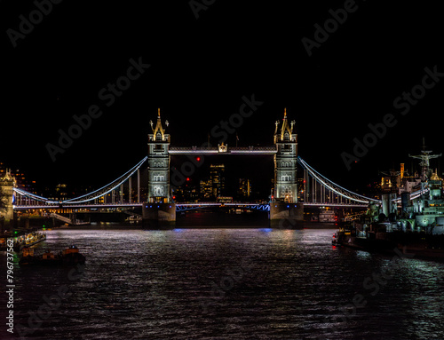 Photography London bus driving past Tower Bridge illuminated at night with illuminated skysc