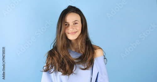 Gorgeous sensual slim tender Caucasian woman in blue pullover shake head, care cosmetics products brunette hair. Girl waving fluttering hair shaking head and fix hair isolated on blue background. photo