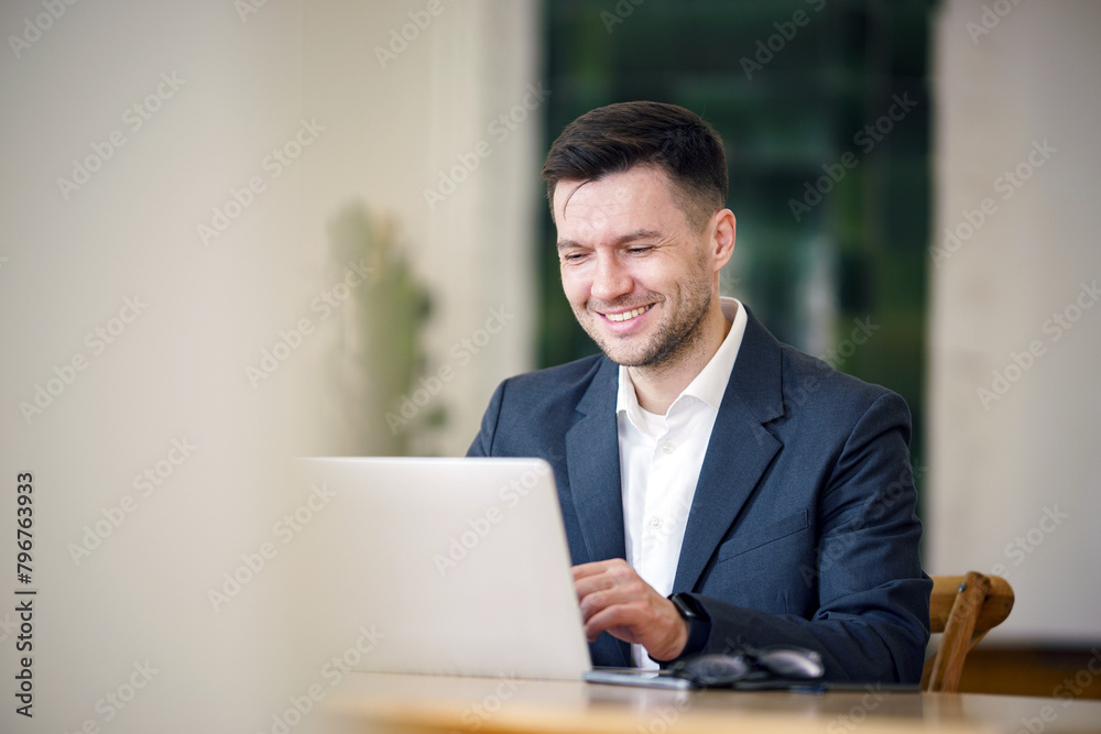 An affable executive savors a moment of satisfaction while working on his laptop in a tranquil, modern office setting. An affable executive savors a moment of satisfaction while working on his laptop in a tranquil, modern office setting.