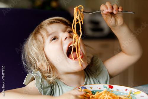 Adorable toddler girl eat pasta spaghetti with tomato bolognese with minced meat. Happy preschool child eating fresh cooked healthy meal with noodles and vegetables at home, indoors.