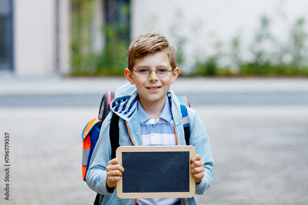 Obraz premium Happy little kid boy with backpack or satchel and glasses. Schoolkid on the way to school. Healthy adorable child outdoors On desk Last day third grade in German. School's out