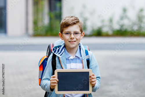 Happy little kid boy with backpack or satchel and glasses. Schoolkid on the way to school. Healthy adorable child outdoors On desk Last day third grade in German. School's out photo