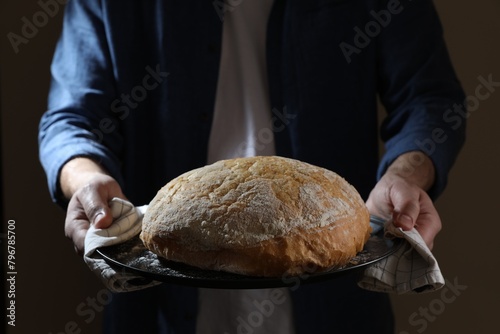 Man holding loaf of fresh bread on dark background, closeup