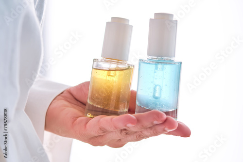 Two yellow and blue serums in a womans hands in a robe.