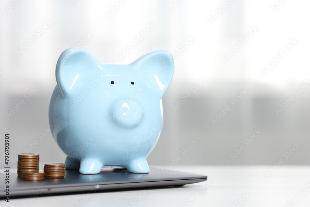 Piggy bank, stacked coins and laptop on white table indoors. Space for text Piggy bank, stacked coins and laptop on white table indoors. Space for text