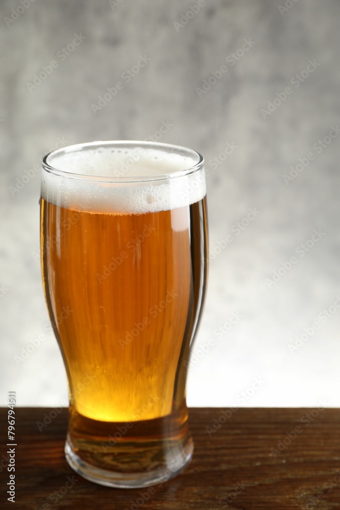 Glass with fresh beer on wooden table against light background Glass with fresh beer on wooden table against light background