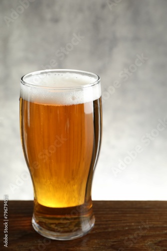 Glass with fresh beer on wooden table against light background