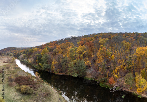 River curve in autumn forest with grey cloudy sky. Wooded riverbanks in moody autumnal aerial