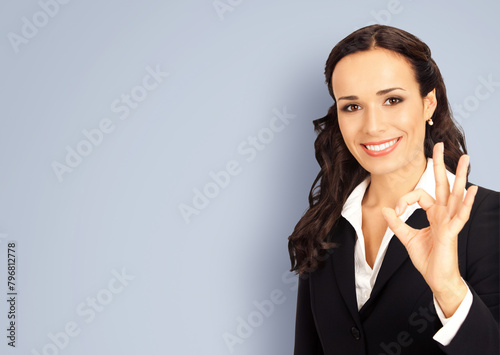 Happy smiling brunette businesswoman business woman wear black confident suit, show okay hand sign gesture, isolated against yellow wall background. Blank empty free ad text area. © vgstudio