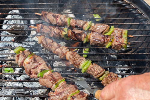 Turning beef brochettes on barbecue with a fork