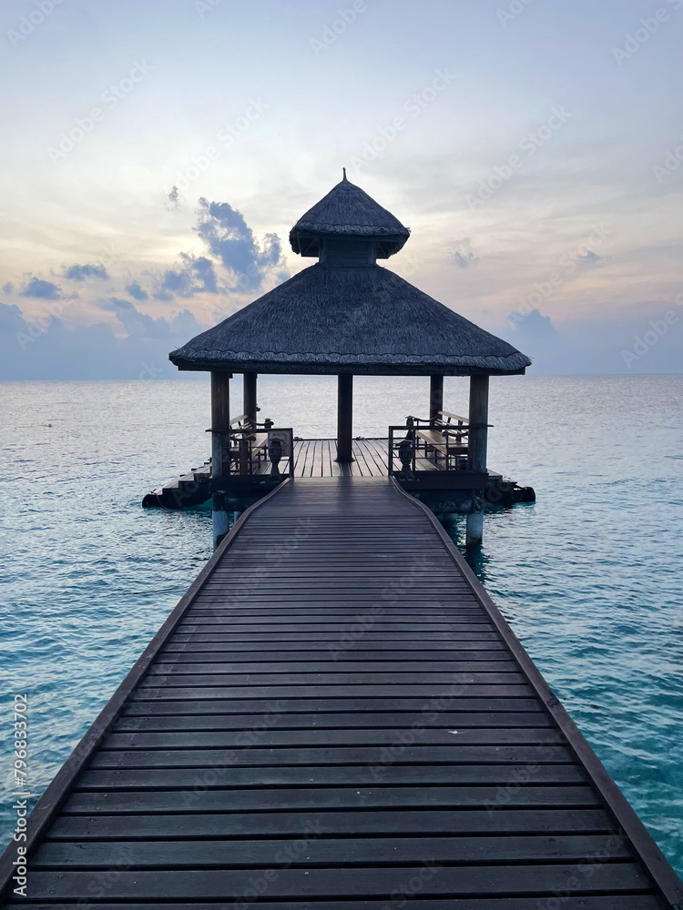 Pier of Maldivian resort at sunrise or sunset, vertical photo 