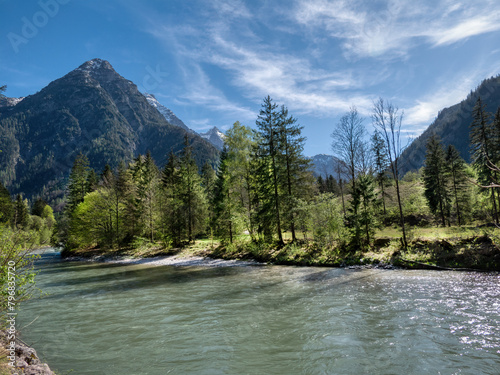 A landscape in the Austrian Alps in spring with a pale blue sky, cirrus clouds, mountains, trees, and a river. Salzburg region