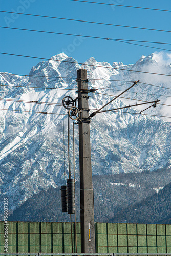 Electric railway installation in front of snow-covered mountains and a blue sky