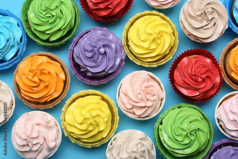 Many tasty cupcakes with bright cream on light blue background, flat lay Many tasty cupcakes with bright cream on light blue background, flat lay
