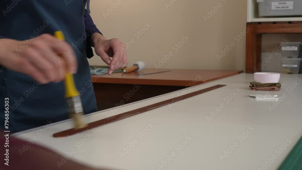 The craftsman uses a brush to coat a leather belt with impregnation. The craftsman uses a brush to coat a leather belt with impregnation.