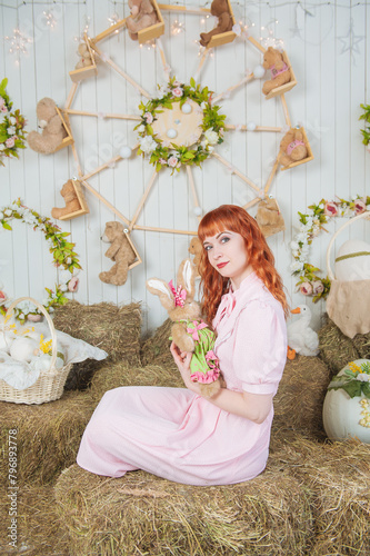 Beautiful redhaired woman with rabbit toy sitting on the haystack Easter holiday concept