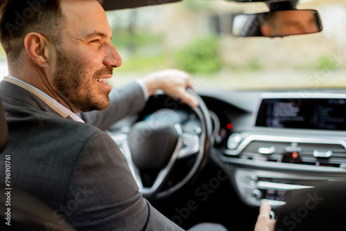 Smiling man enjoying a sunny drive in a modern car interior © BGStock72