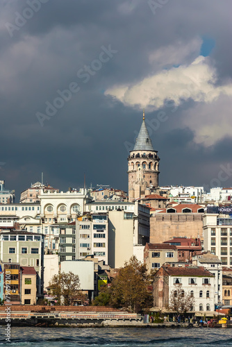 The Galata Tower stands tall amidst the modern Istanbul skyline under a dramatic cloud-filled sky. Istanbul, Turkey (Turkiye)