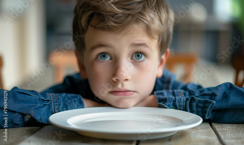 A young boy looking at his empty plate with a look of hunger and longing in his eyes. This image is a powerful reminder of the problem of malnutrition and hunger that affects many children.