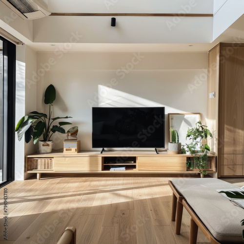 A living room with a wooden entertainment center and a black flat screen television. The room is bright and airy  with a large window letting in plenty of natural light